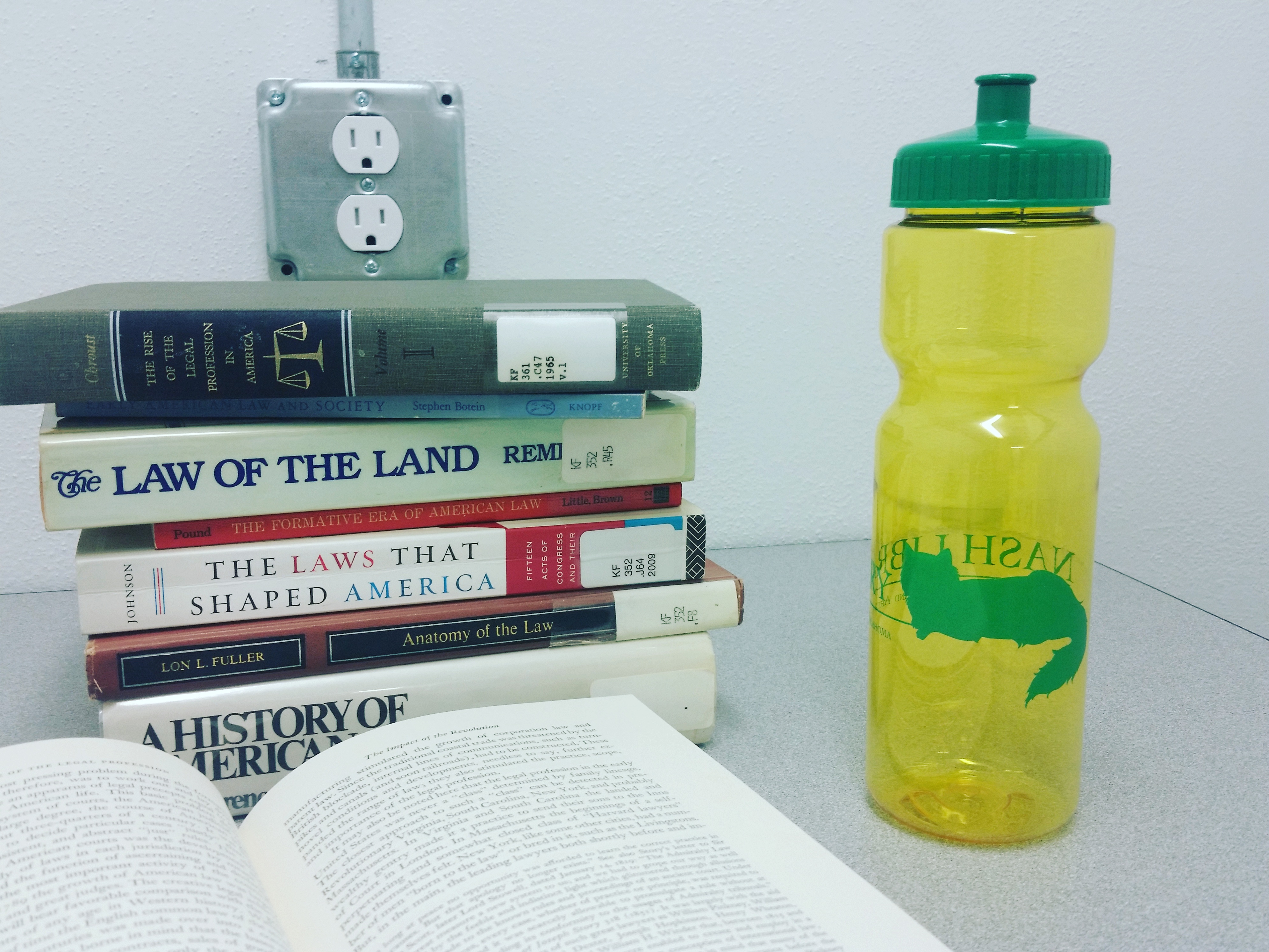 on a desk, yellow water bottle with a green lid next to stack of books. There is a cat logo on the water bottle.